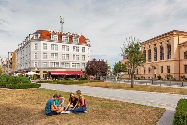 Junge Menschen sitzen auf der Wiese am Platz am Stern. Im Hintergrund ist das Hotel Kaiserhof sowie die Rahn-Schule zu sehen. 